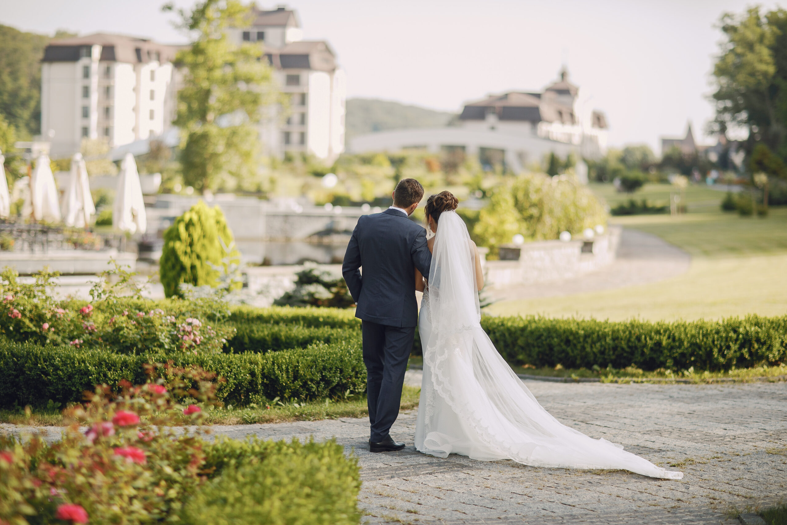 A young and beautiful bride and her husband is standing in a summer park with bouquet of flowers